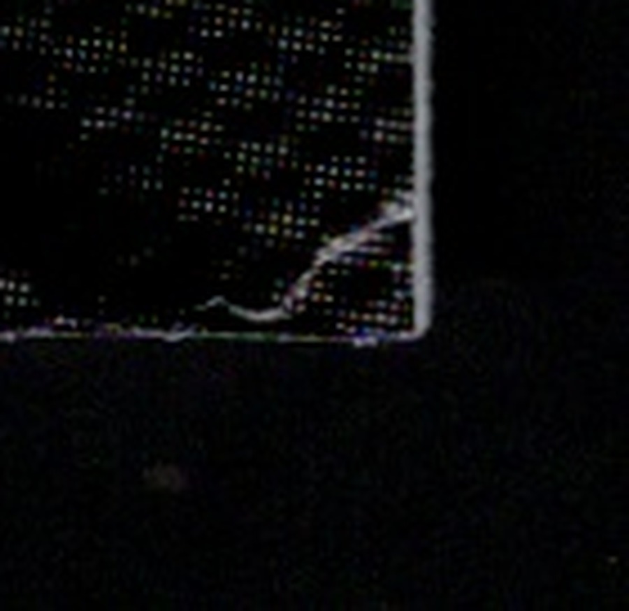 Magnified back bottom-right corner: a curved white tear across the black surface at the tip